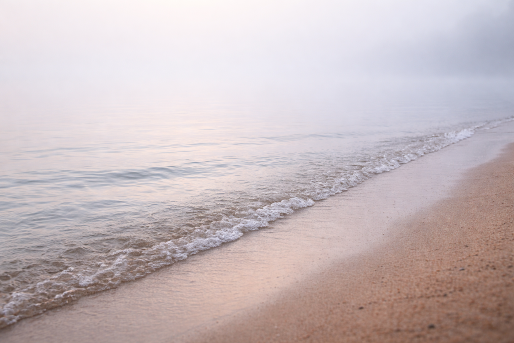 Kirjeitä veden äärellä-I Ranta 1 Hiekan ja veden rajapinta sumuisessa järvimaisemassa,ilman horisonttia
