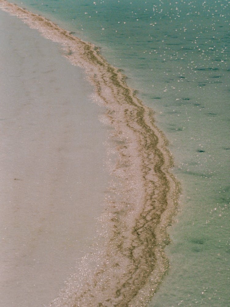 Hiekkaranta veden reunassa,jäljet häviämässä aaltojen alle